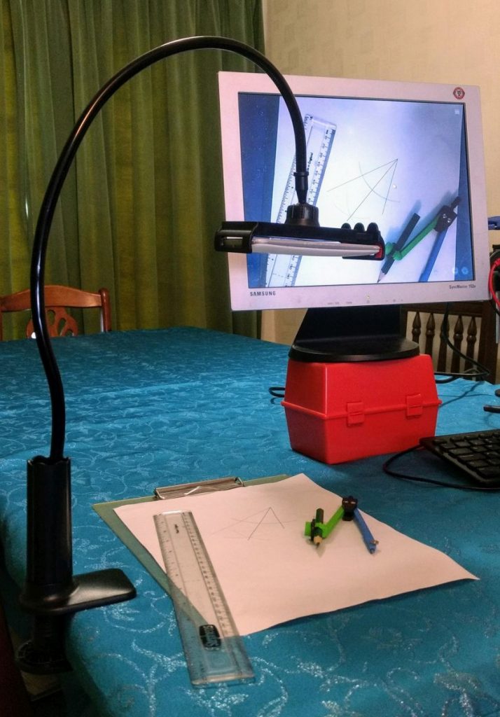 DIY visualiser in use: a smartphone mounted in a gooseneck stand attached to the table edge by a G-clamp, and a computer monitor showing the camera output.