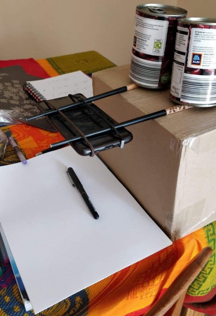 Smartphone suspended from a pair of chopsticks held in place by food tins balanced on top of a box